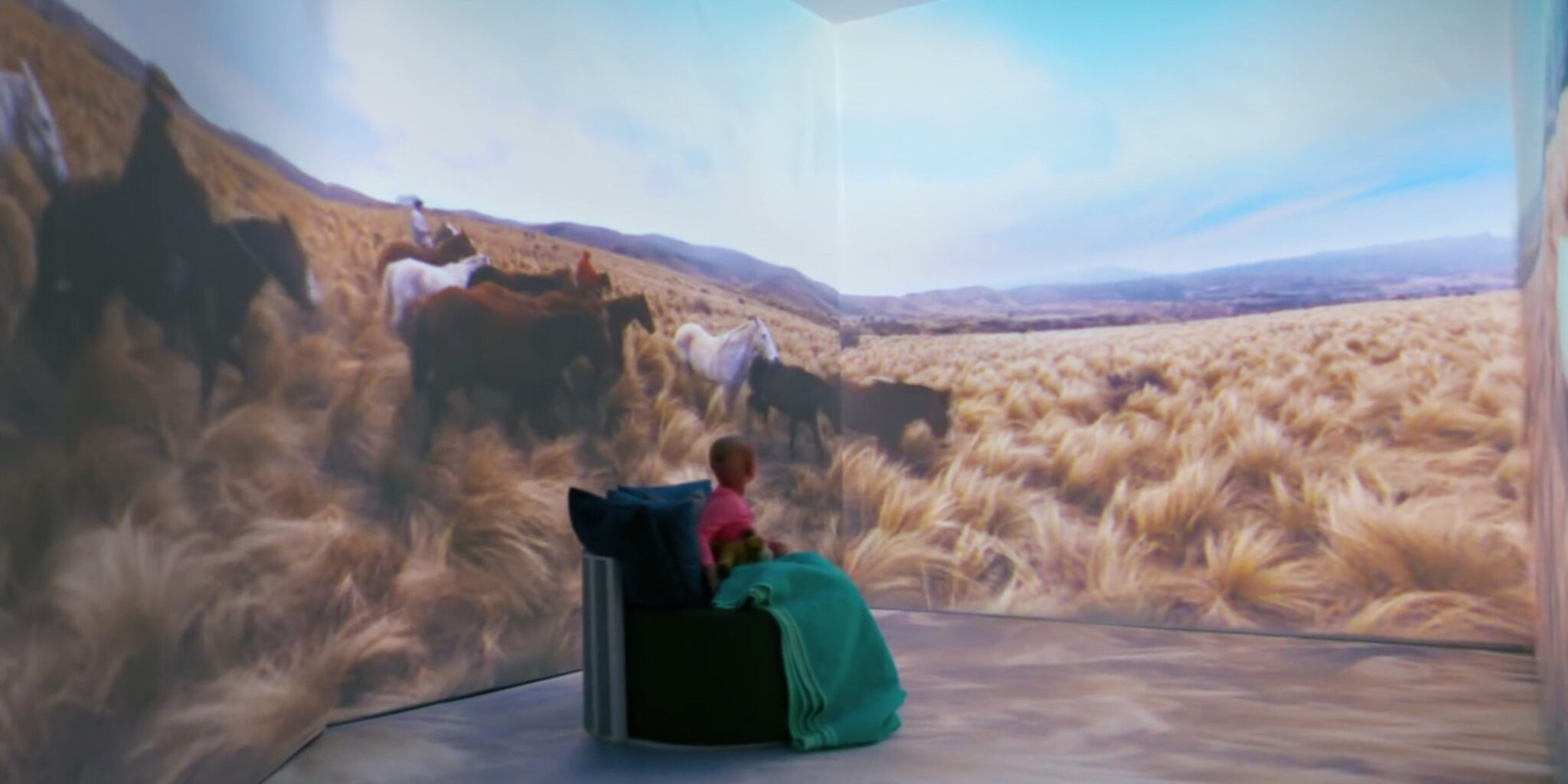 A St. Jude patient inside the Dream Adventures immersive room, watching wild horses run across the projected Argentine grasslands.